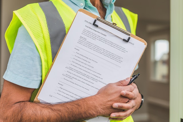 Person in yellow reflective safety vest holding a pren and a clipboard with a checklist